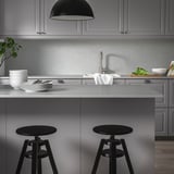 Modern kitchen with grey LOCKEBO recycled glass countertops, black round stools, sleek appliances, and minimalist design.