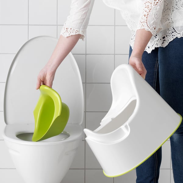 Adult places lime green and white childrens toilet seat into white toilet for training.