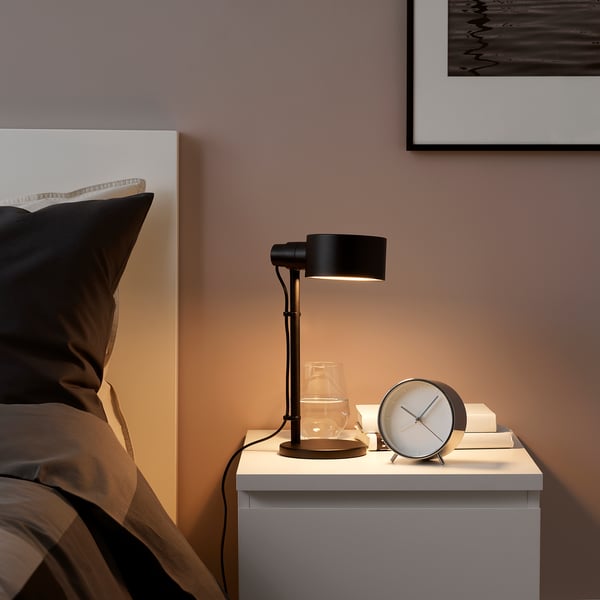 A LÖVMÅNAD lamp on bedside table, adjustable, next to water glass and alarm clock.