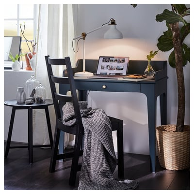 Blue LOMMARP desk with pull-out drawer, black chair, grey blanket, white wall, lamp, plant.