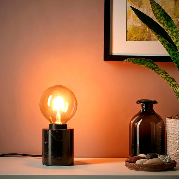 A small lamp on a table with a warm light bulb radiates a cozy glow.
