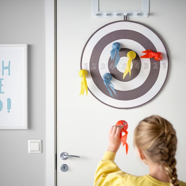 Girl playing colorful dart game on door target with fish fasteners.