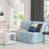 Modern living room with blue & white sofa-bed, colorful cushions, coffee table, rug, and plant. Dark curtains frame large window.