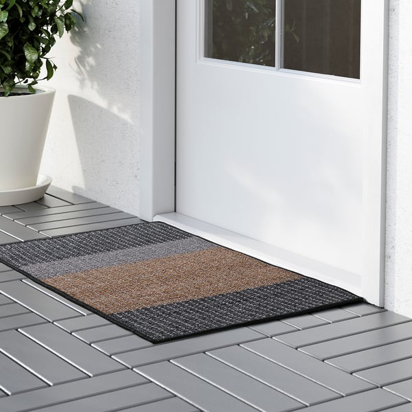 Door mat with uneven, striped surface outside home entrance, catching dirt and adding texture.