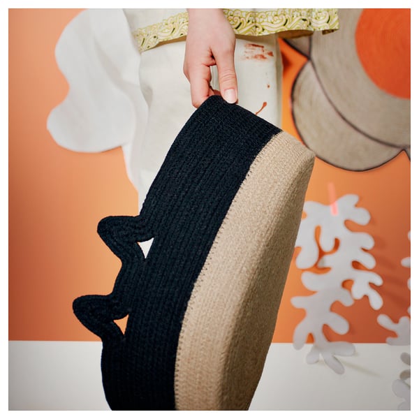 Hand holds striped black and beige MÄVINN basket. Basket has braided jute and cotton design, sits against vibrant, abstract wall.