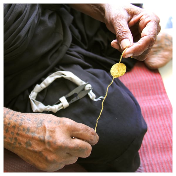 Crafting yellow item with thread, scissors, rings. Black attire, tattooed.