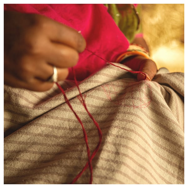 A person hand-stitching a red and beige cushion cover with a heart design.