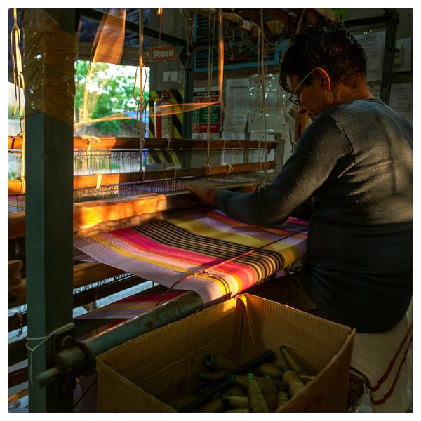 Woman weaving colorful striped fabric on a loom.