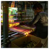 Woman weaving colorful striped fabric on a loom.