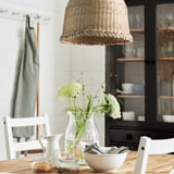 Beige MÄVINN lampshade over wooden dining table with vase, pitcher, and towels.