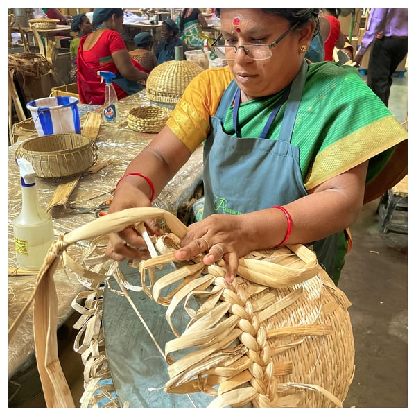 Woman crafting wicker basket with banana fibers, surrounded by tools.