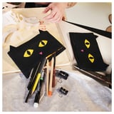Black cat-shaped pouch with yellow eyes and colorful nose, holding pens. IKEA MÄVINN, 100% cotton, hand on zipper.