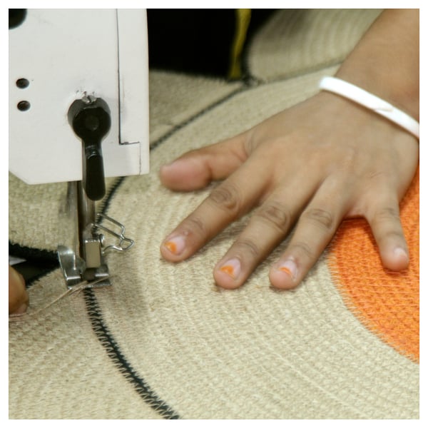 Person using sewing machine to stitch jute fabric. Close-up shows hand guiding material under needle.