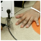 Person using sewing machine to stitch jute fabric. Close-up shows hand guiding material under needle.