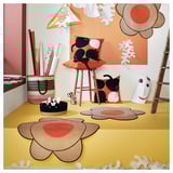 Bright, yellow room with MÄVINN flower-shaped rugs in brown and orange. Decorated with cat pillows, wall hangings, and a basket.