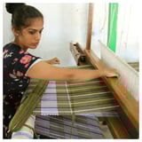 Young woman operating a traditional weaving loom, crafting a multicolored striped rug, showcasing manual textile artistry.