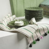 Green and white table runner with tassels, displaying small plate and cheese garnished with herbs.