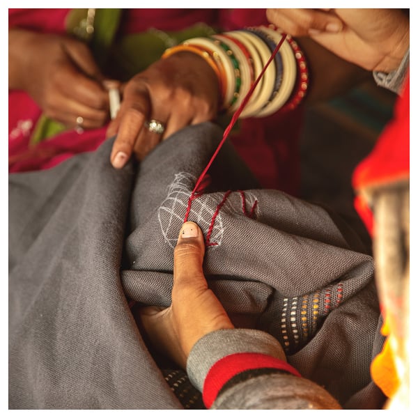 People holding a red thread wrapped around a hand, adorned with colorful bangles.