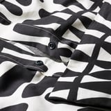 Close-up of a duvet cover with a natural leaf pattern, featuring two black press-stud fasteners for fastening.