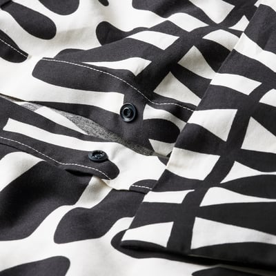 Close-up of a duvet cover with a natural leaf pattern, featuring two black press-stud fasteners for fastening.