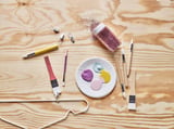 Art supplies: brushes, palette, paint, glitter on wooden table.