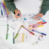 Childs hands using colorful markers to draw on paper, surrounded by various colors and art supplies, symbolizing creativity and imagination.