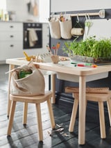 Childs play table with wooden chairs, featuring a plant, art supplies, and hanging organizers.