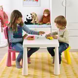 Kids play with colorful dough on white table, pink stools. Stuffed animals nearby on blue bench.