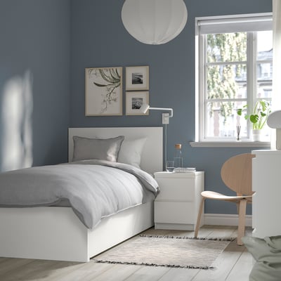 Modern bedroom with MALM bed, gray bedding, blue wall, nightstand, lamp, art, and wooden chair by window.