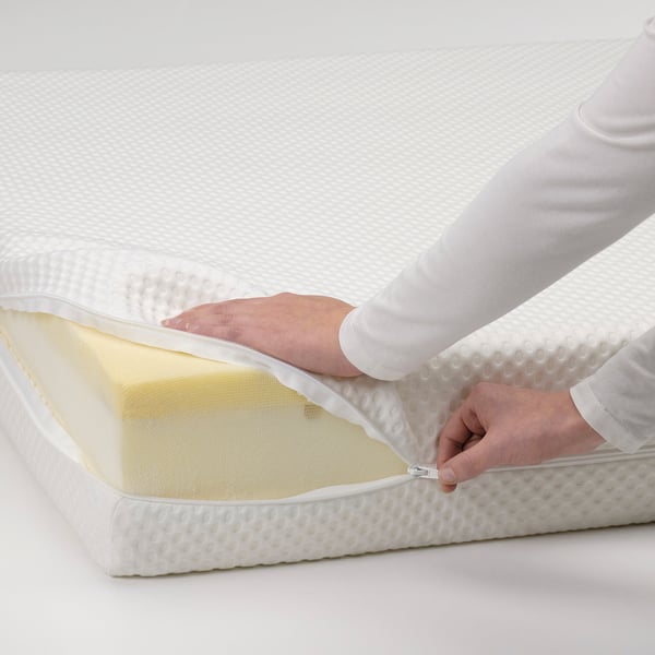 Person zips mattress protector onto white mattress.