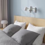 Blue bedroom with wooden bed, pillows, and side lamp.