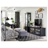 Modern living space with gray floral sofa, black tv stand, patterned rug, and dining area with wicker chairs and black table.