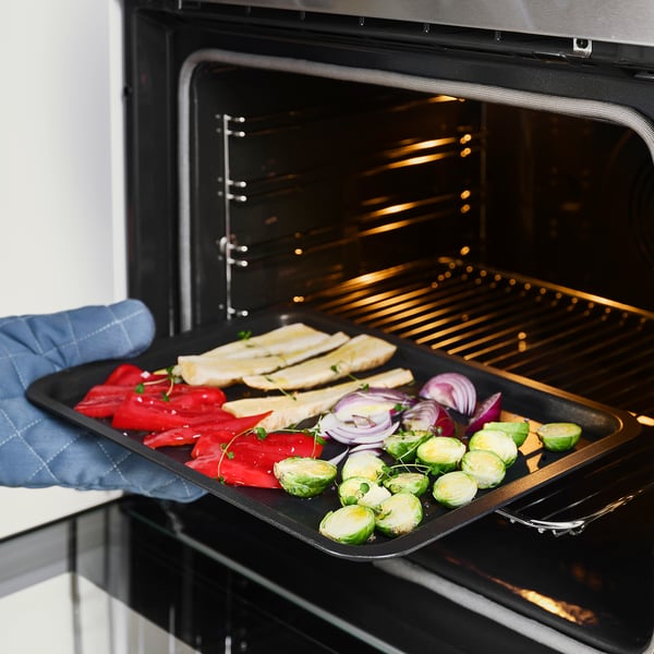 Person placing oven tray with vegetables into oven.