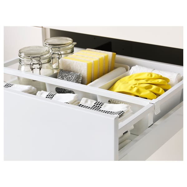 White kitchen drawer fully out, showing cleaning supplies like sponges, gloves, and jars with towels.