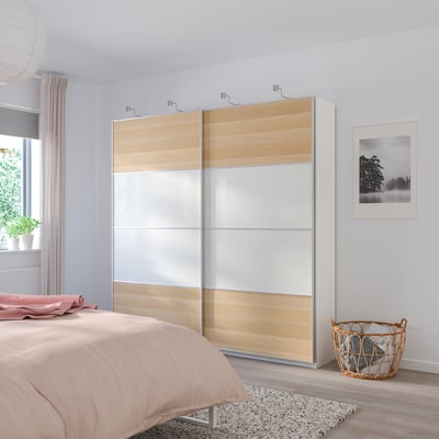 Modern bedroom with large MEHAMN wardrobe. Light wood and white, sliding mirrored doors. Window with curtains and plant adds natural light.