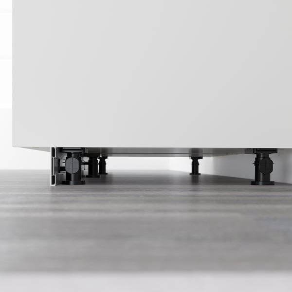 Black adjustable legs supporting white cabinet for stability on uneven floors.