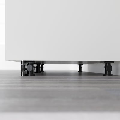 Black adjustable legs supporting white cabinet for stability on uneven floors.