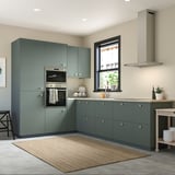 Modern kitchen with green-gray cabinets, sleek handles, built-in oven, and a rug.