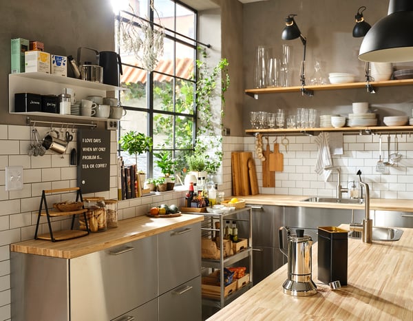 Modern industrial kitchen with stainless-steel gray cabinets, wooden countertops, open shelves, and hanging lights.