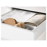 White kitchen drawer with cork trivet and cloth, showcasing an organized, minimalist arrangement.