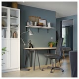 A grey ikea MITTCIRKEL desk setup in a blue room. It a light pine-like top and adjustable chair, with a bookshelf and lamp nearby.