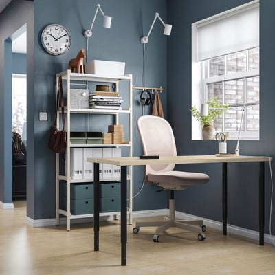 Home office setup with MITTCIRKEL desk in pine, light-colored chair, wall clock, and shelving unit with various items, all against blue-gray walls.