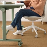 Person sits at adjustable desk on ergonomic chair with footrest, notes in hand.