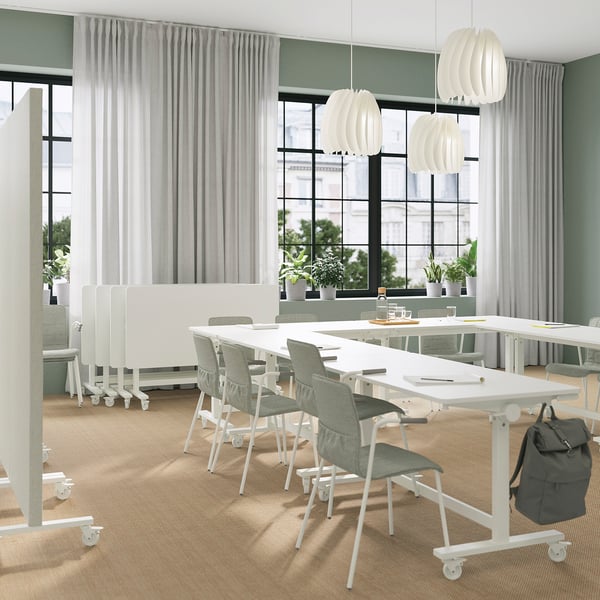 Modern office with MITTZON foldable tables, gray chairs, big windows, pendant lamps, and a backpack.