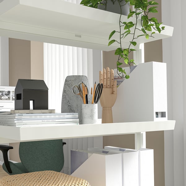 A modern office division system with shelves displaying books, a wooden hand, and plants; portable with castors.