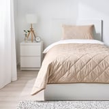 Light bedroom: white bed, beige bedding, nightstand, lamp, clock, window, rug