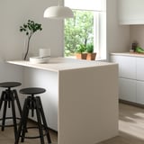 Modern kitchen island with white MÖCKLARP porcelain top, black stools, plates, and greenery.