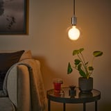 Cozy corner: hanging bulb, beige throw, glass table, warm light.