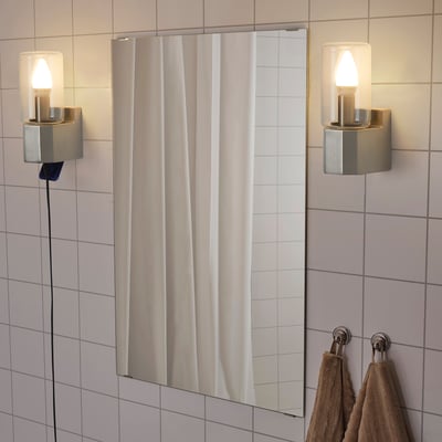 Modern bathroom with white tiles, MOLNSLAG lamps, gold bodies, warm light, and hanging towels.