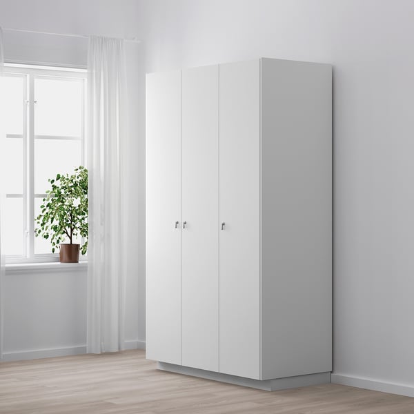 Minimalist white cabinet with silver drop handles, positioned near a window with sheer curtains. A potted plant sits on the windowsill.